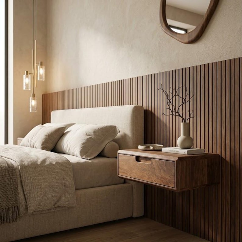 Puede incluir: Un dormitorio con una cama tapizada en beige, almohadas a juego y una manta. Una mesita de noche flotante de madera est&aacute; montada en una pared de listones verticales de color marr&oacute;n oscuro. Un jarr&oacute;n de cer&aacute;mica con ramas descansa sobre ella.