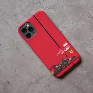 May include: Red phone case with a Formula 1 race car design. The case has a black stripe and the name "CHARLES LECLERC" with a signature and a Ferrari logo. The case is designed for a smartphone.