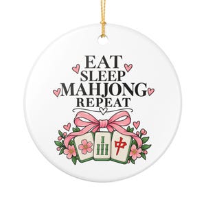 Może przedstawiać: Okrągła biała ceramiczna ozdoba z czarnym napisem EAT SLEEP MAHJONG REPEAT i małymi różowymi sercami. Poniżej tekstu znajdują się trzy płytki mahjong ozdobione różową kokardą, zielonymi liśćmi i różowymi kwiatami wiśni, zawieszone na złotym sznurku.