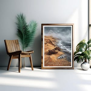 Könnte beinhalten: Ein gerahmter Druck, der die Skeleton Coast in Namibia zeigt. Das Kunstwerk zeigt zwei Schiffswracks an einem Sandstrand mit einem Walskelett. Der Text "SKELETON COAST NAMIBIA" ist sichtbar. Der Druck ist in einem Holzrahmen.