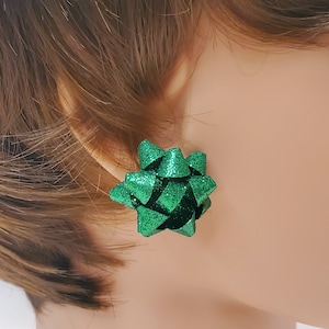 May include: A pair of green glitter bow earrings. The bows are made of a sparkly green material and are shaped like a traditional bow.