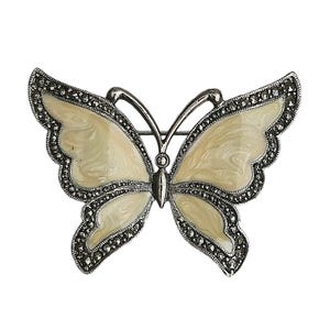 May include: A silver butterfly brooch with a white enamel body and a detailed marcasite design.