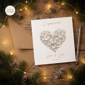 Personalized wedding card displayed in a warm, cozy Christmas holiday setting with fairy lights and pine.