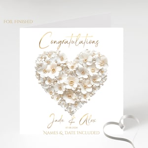 A white square card with a gold foil border and the words "FOIL FINISHED" in the top left corner, featuring a heart shape made of white flowers and pearls, with "Congratulations" in gold foil above and "Jade & Alex" and "07.08.2026" and "NAMES &