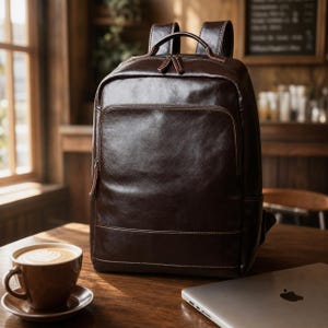 May include: A dark brown leather backpack featuring a smooth finish, a large main compartment with a top zip, a smaller front zipped pocket, two adjustable shoulder straps, and a top handle, all accented with matching brown stitching.