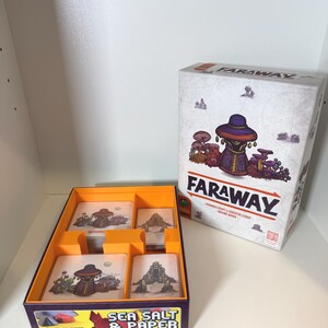 May include: A board game called "FARAWAY" is shown, with its box and contents visible. The box has illustrations of fantasy figures and mushrooms. Inside, a purple and orange tray holds cards with matching artwork. The game is "Sea Salt & Paper."