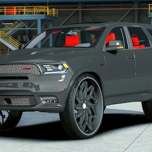 Puede incluir: Un SUV gris oscuro con interior rojo y grandes ruedas negras personalizadas. La parrilla delantera tiene un emblema rojo. El vehículo está estacionado en un almacén con equipo industrial en el fondo.