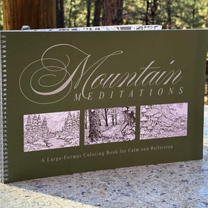May include: A spiral-bound coloring book titled "Mountain Meditations" with a green cover. The cover features the title in elegant script above three landscape illustrations. The text "A Large-Format Coloring Book for Calm and Reflection" is below.