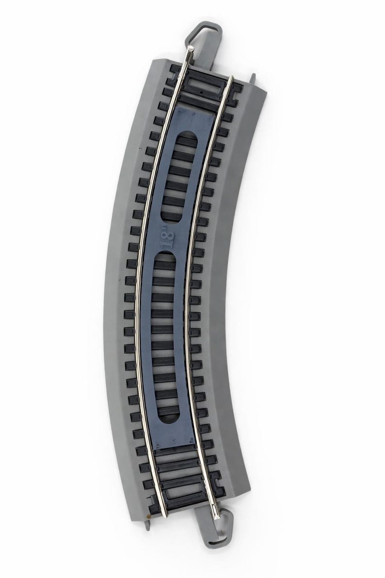 Op de afbeelding: Gebogen grijs plastic treinspoorsectie met zilveren metalen rails. De baan heeft een donkerblauw middengedeelte met het nummer "18" erop gedrukt. De baan is ontworpen om verbinding te maken met andere baanonderdelen.