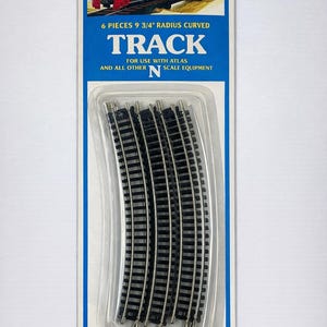 May include: Pack of six curved N scale model railway tracks with a 24.77 cm radius. The packaging features a red train illustration and the text "TRACK". Suitable for ages 8 and up.