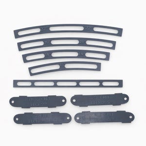 Op de afbeelding: Een verzameling donkergrijze, gebogen en rechte plastic stukken met verschillende lengtes en tekst. De gebogen stukken zijn gemarkeerd met afmetingen van 38,1 cm tot 55,9 cm. Kleinere stukken hebben tekst zoals "HO 2" en "HO 2.5".