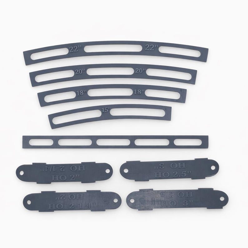 Op de afbeelding: Een verzameling donkergrijze, gebogen en rechte plastic stukken met verschillende lengtes en tekst. De gebogen stukken zijn gemarkeerd met afmetingen van 38,1 cm tot 55,9 cm. Kleinere stukken hebben tekst zoals "HO 2" en "HO 2.5".