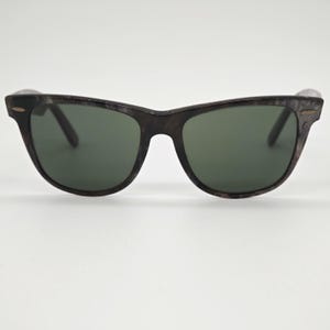 Puede incluir: Gafas de sol con montura oscura con vetas de madera y lentes verde oscuro. Las gafas tienen un dise&ntilde;o cl&aacute;sico y atemporal, adecuado para varios estilos. Las lentes ofrecen protecci&oacute;n contra el resplandor solar.