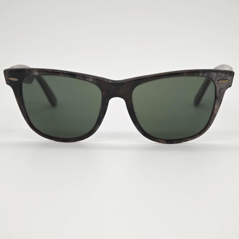 Puede incluir: Gafas de sol con montura oscura con vetas de madera y lentes verde oscuro. Las gafas tienen un dise&ntilde;o cl&aacute;sico y atemporal, adecuado para varios estilos. Las lentes ofrecen protecci&oacute;n contra el resplandor solar.