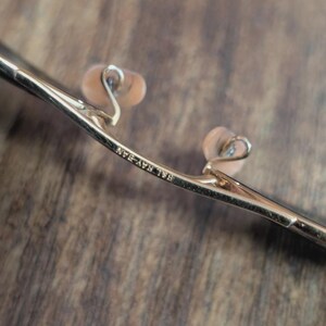 May include: Close-up of a pair of gold-colored eyeglasses. The nose pads are a light peach color. The text "Ray-Ban" is visible on the frame.