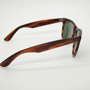 May include: Tortoiseshell-patterned sunglasses with green lenses. The sunglasses have a classic design with a dark brown and amber color scheme. The Ray-Ban logo is visible on the right arm.