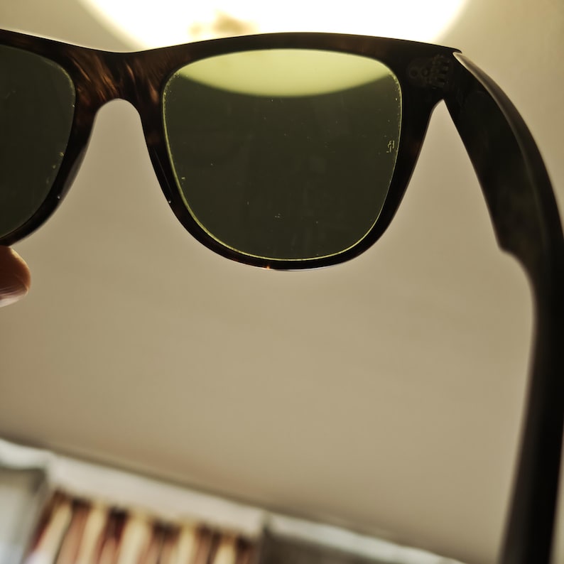 Puede incluir: Gafas de sol con montura oscura y lentes verdes. Las monturas tienen un patr&oacute;n marr&oacute;n veteado. Las lentes son de color verde claro. Las gafas de sol se sostienen sobre un fondo claro.