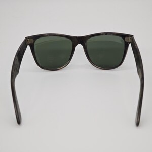 Puede incluir: Gafas de sol con montura oscura y veteada y lentes verdes. El cl&aacute;sico estilo Wayfarer presenta una forma rectangular y patillas gruesas. Las gafas de sol est&aacute;n dise&ntilde;adas para proteger los ojos del sol.