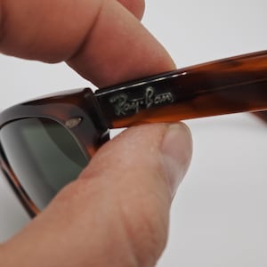May include: Close-up of Ray-Ban sunglasses with a tortoiseshell pattern. The frame is brown and black with the Ray-Ban logo in silver. The lenses are a dark green color.