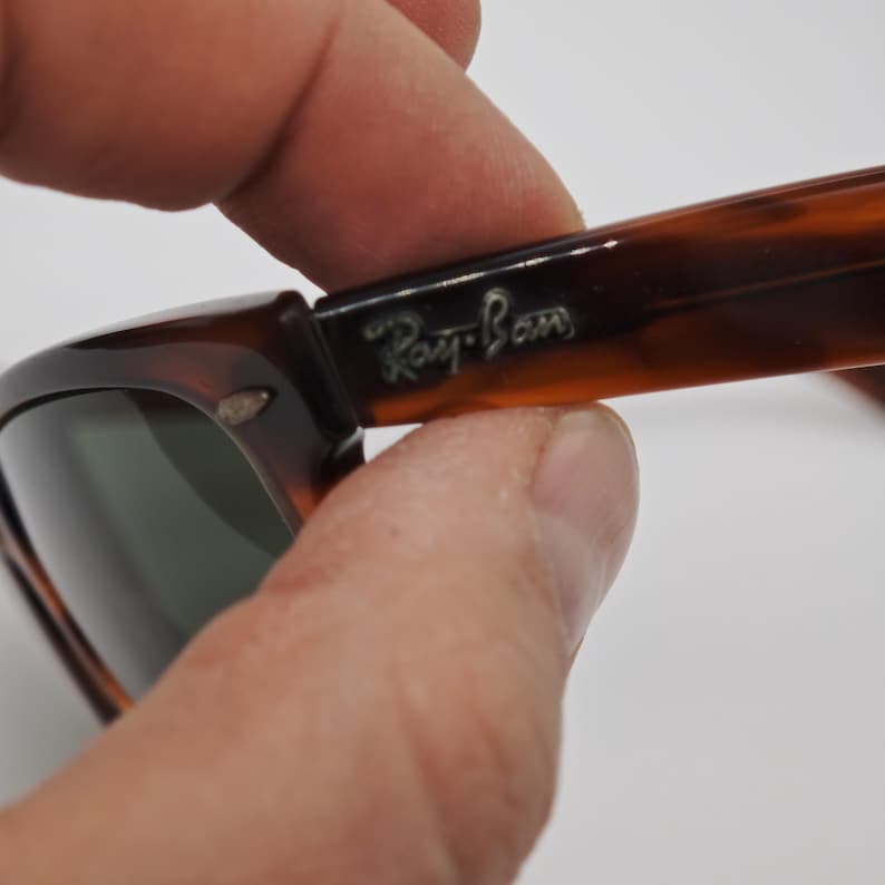 May include: Close-up of Ray-Ban sunglasses with a tortoiseshell pattern. The frame is brown and black with the Ray-Ban logo in silver. The lenses are a dark green color.