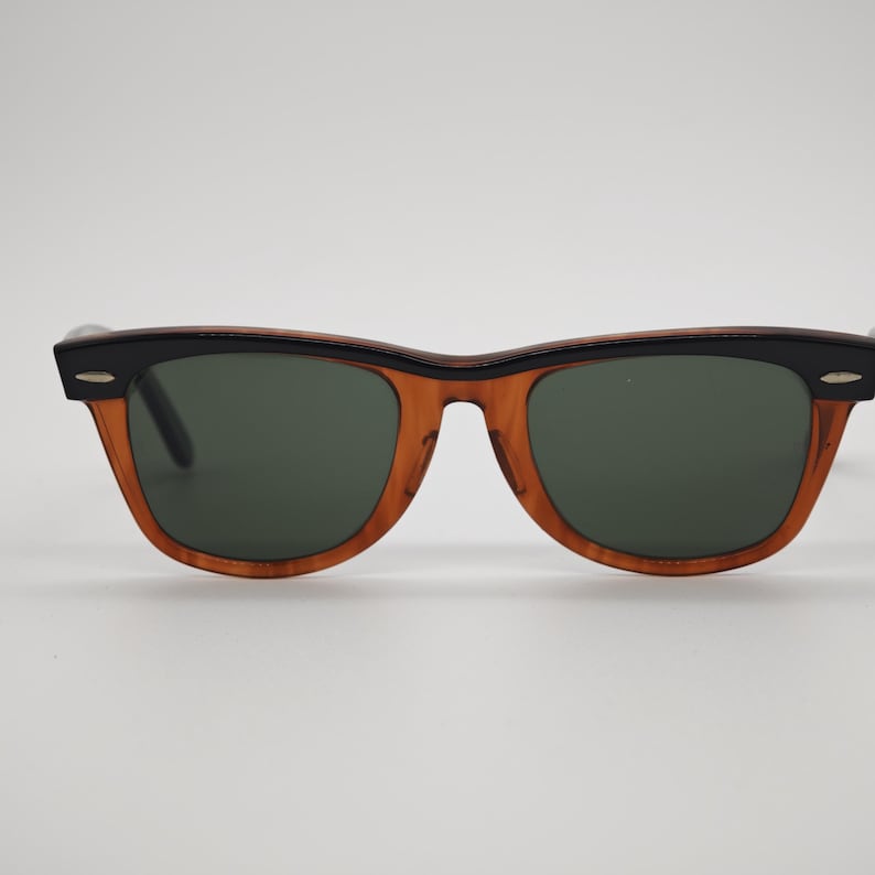 May include: Sunglasses with a classic design. The frames are a warm brown color with black accents on the top and temples. The lenses are a dark green color, providing a stylish and functional accessory.