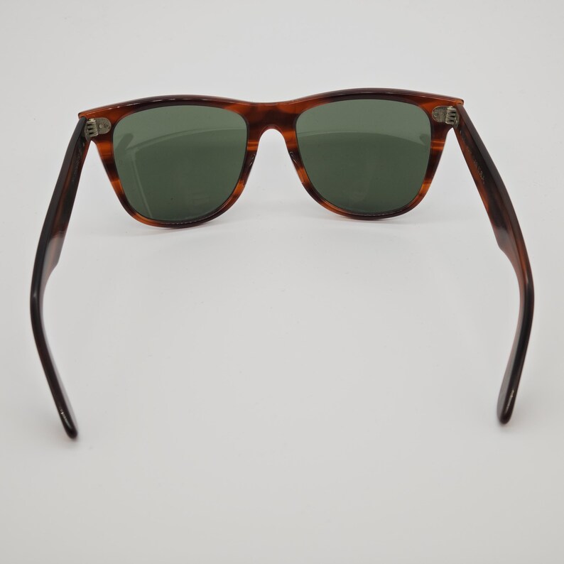 May include: Brown tortoiseshell sunglasses with green lenses. The classic frame design features a rectangular shape and dark brown temples. The sunglasses are displayed against a white background.