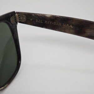 Puede incluir: Primer plano de unas gafas de sol con montura oscura y lentes verdes. El texto "B&L RAY-BAN U.S.A." est&aacute; impreso en la patilla. La montura tiene un patr&oacute;n moteado.