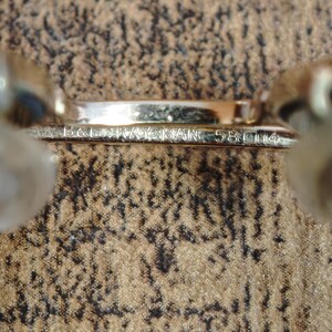 May include: Close-up of a gold-colored metal frame with the engraved text "B&L RAY-BAN 58[]14". The frame is set against a textured, brown and black patterned background. The image focuses on the details of the frame.