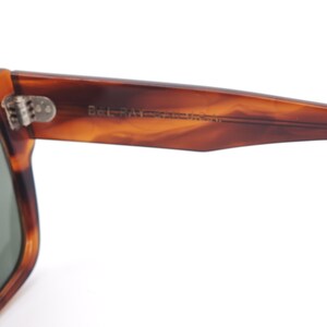 May include: Close-up of a pair of sunglasses with a brown tortoiseshell frame. The arm of the sunglasses has the text "Bel-Ray" printed on it. The sunglasses have a silver hinge.