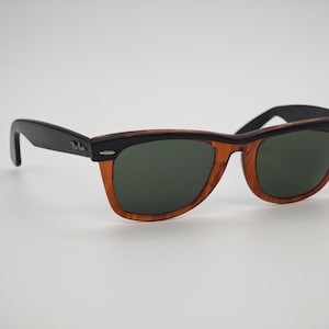 May include: Sunglasses with a black frame and temples, and a brown and black patterned frame. The lenses are a dark green color. The sunglasses are set against a white background.