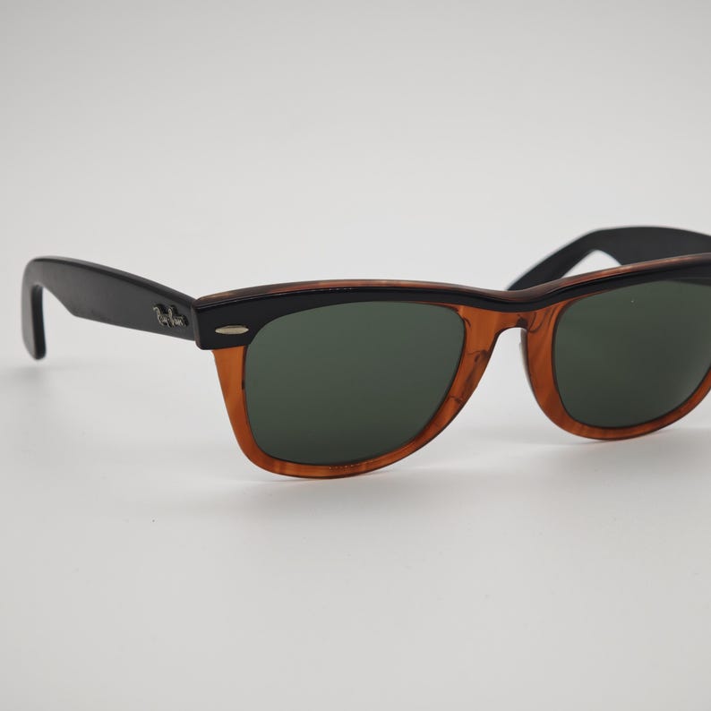 May include: Sunglasses with a black frame and temples, and a brown and black patterned frame. The lenses are a dark green color. The sunglasses are set against a white background.