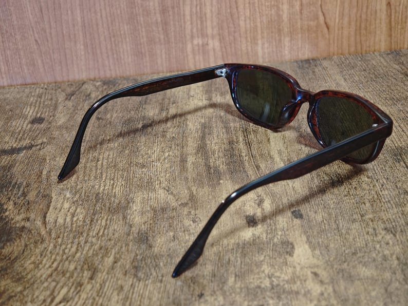 May include: Sunglasses with dark lenses and a tortoiseshell pattern frame. The arms are a dark brown color. The sunglasses are resting on a wooden surface.