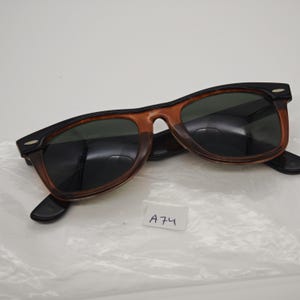 May include: Sunglasses with a black and brown frame and dark lenses. The sunglasses have a classic design with a rectangular shape. The lenses are dark green. The frame is a combination of black and brown.
