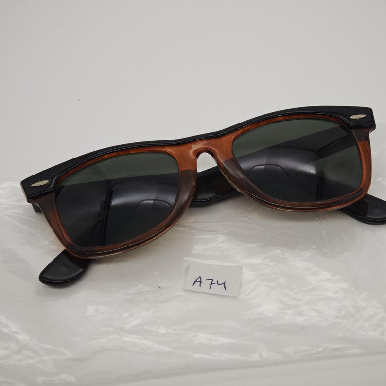 May include: Sunglasses with a black and brown frame and dark lenses. The sunglasses have a classic design with a rectangular shape. The lenses are dark green. The frame is a combination of black and brown.