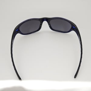 May include: Dark blue sunglasses with dark grey lenses. The sunglasses have a curved frame and temples, and are set against a white background. The sunglasses are designed for outdoor use.