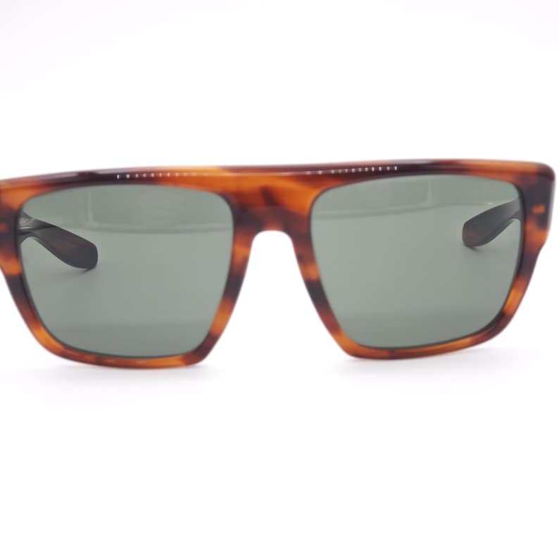 May include: Tortoiseshell-patterned sunglasses with a square frame and dark green lenses. The sunglasses have a classic design with a thick frame and a subtle, curved bridge. The temples are dark and sleek.