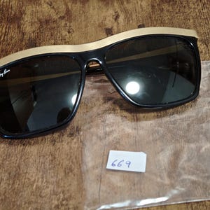 Peut inclure: Lunettes de soleil noires avec une monture sup&eacute;rieure dor&eacute;e. Les lunettes ont des verres fonc&eacute;s et une forme rectangulaire. Le logo Ray-Ban est visible sur la lentille gauche. Une petite &eacute;tiquette blanche avec le num&eacute;ro 669 est &eacute;galement pr&eacute;sente.