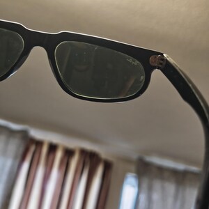 May include: Black sunglasses with dark lenses. The frames are thick and rectangular. The Ray-Ban logo is visible on the temple. The sunglasses are angled, showing the lenses and part of the frame.