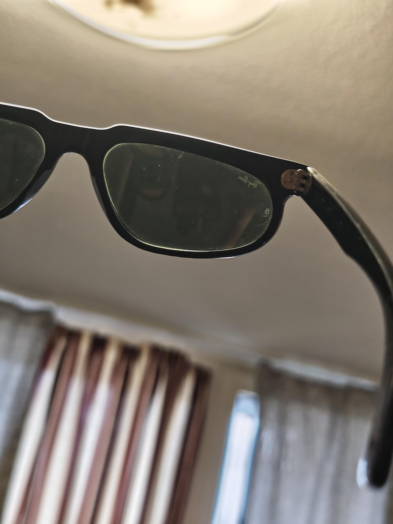 May include: Black sunglasses with dark lenses. The frames are thick and rectangular. The Ray-Ban logo is visible on the temple. The sunglasses are angled, showing the lenses and part of the frame.