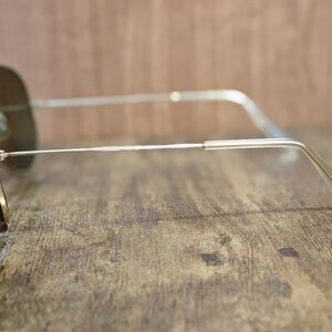 May include: Aviator-style sunglasses with a silver metal frame and dark lenses. The sunglasses are resting on a wooden surface, showcasing the sleek design and classic shape. The lenses appear to be tinted, offering a stylish look.