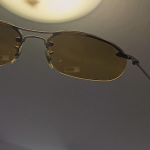 May include: Rimless sunglasses with a gold-colored metal frame and amber-tinted lenses. The sunglasses have a classic design with a double bridge and thin temples. The lenses are oval-shaped and provide a warm, golden hue.