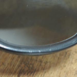 May include: Close-up of a black, circular object with a reflective surface. The object has a thin, dark rim and appears to be made of glass or a similar material. The background is a wooden surface.