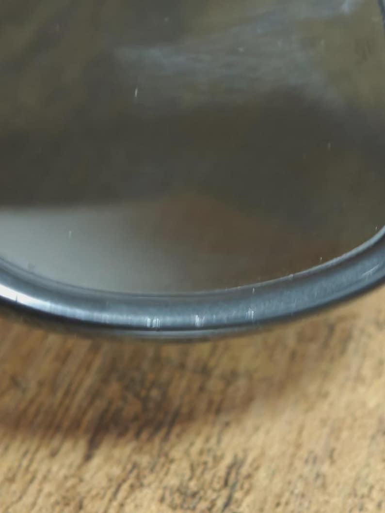 May include: Close-up of a black, circular object with a reflective surface. The object has a thin, dark rim and appears to be made of glass or a similar material. The background is a wooden surface.