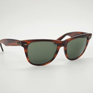 May include: Classic tortoiseshell sunglasses with dark green lenses. The frames have a brown and black pattern, and the temples are slightly curved. The sunglasses are set against a white background.