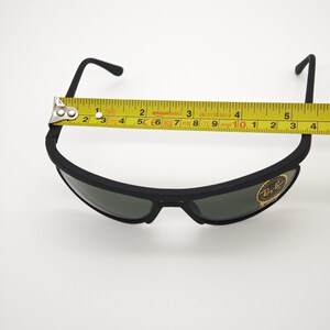 May include: Black Ray-Ban sunglasses with a yellow measuring tape showing a width of approximately 12.7 cm. The sunglasses have dark lenses and a matte black frame. The Ray-Ban logo is visible on the lens.