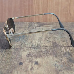May include: Gold-tone aviator sunglasses with dark lenses. The sunglasses have a classic teardrop shape, a thin gold metal frame, and black temple tips. The lenses appear to be tinted, offering a sleek, vintage aesthetic.