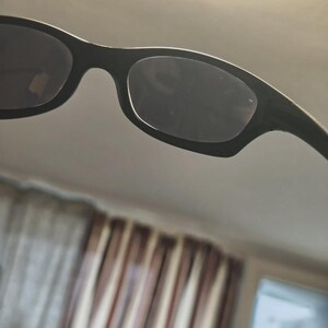 May include: Black sunglasses with a rectangular frame and dark lenses. The sunglasses have a sleek, modern design, suitable for various outdoor activities. The frame appears to be made of a durable material, offering both style and protection from the sun.