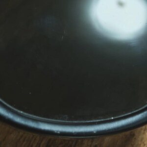 May include: Close-up of a black, circular object with a glossy finish. The object has a slightly raised edge and reflects a bright light source. The background is a wooden surface.
