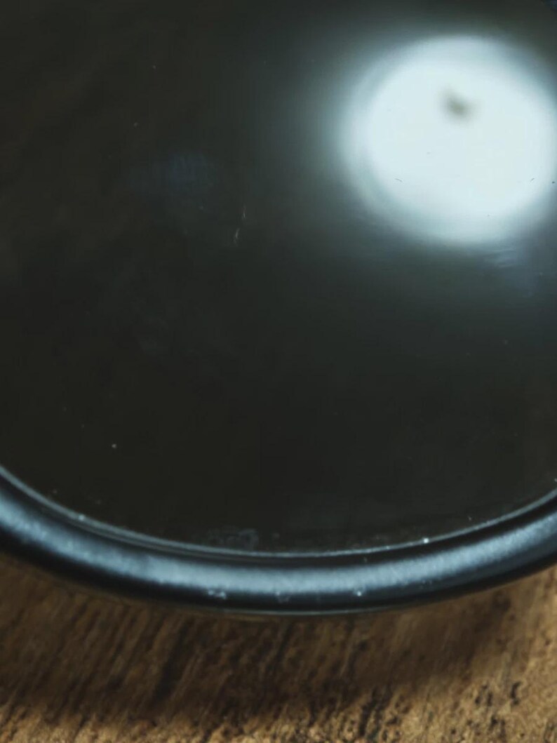 May include: Close-up of a black, circular object with a glossy finish. The object has a slightly raised edge and reflects a bright light source. The background is a wooden surface.