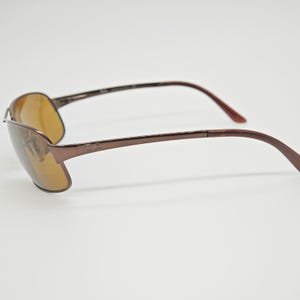 May include: Brown sunglasses with a metallic frame and amber-tinted lenses. The sunglasses have a sleek, modern design with curved temples and a subtle logo on the arm. The lenses are a warm, light brown color.